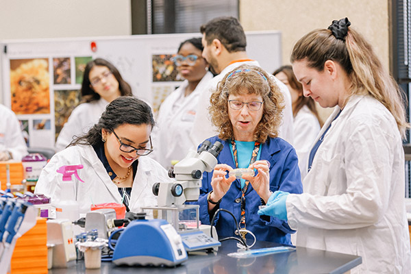 Professor and students in lab coats examining a sample with a microscope