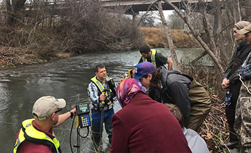 USGS staff explaining how to operate a streamflow gauge to students by a river