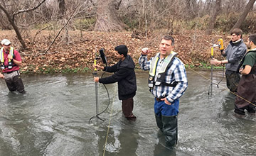 Alternate view of USGS staff explaining how to operate a streamflow gauge to students by a river