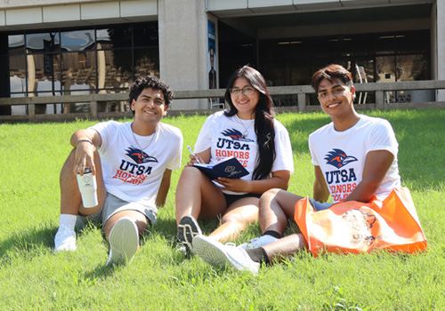 three student sitting on campus grass