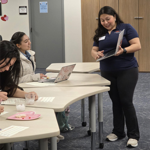 standing student showing seated students something on a laptop