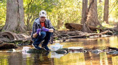 Ronny Saunders perches on a rock to conduct water quality research at Cibolo Creek